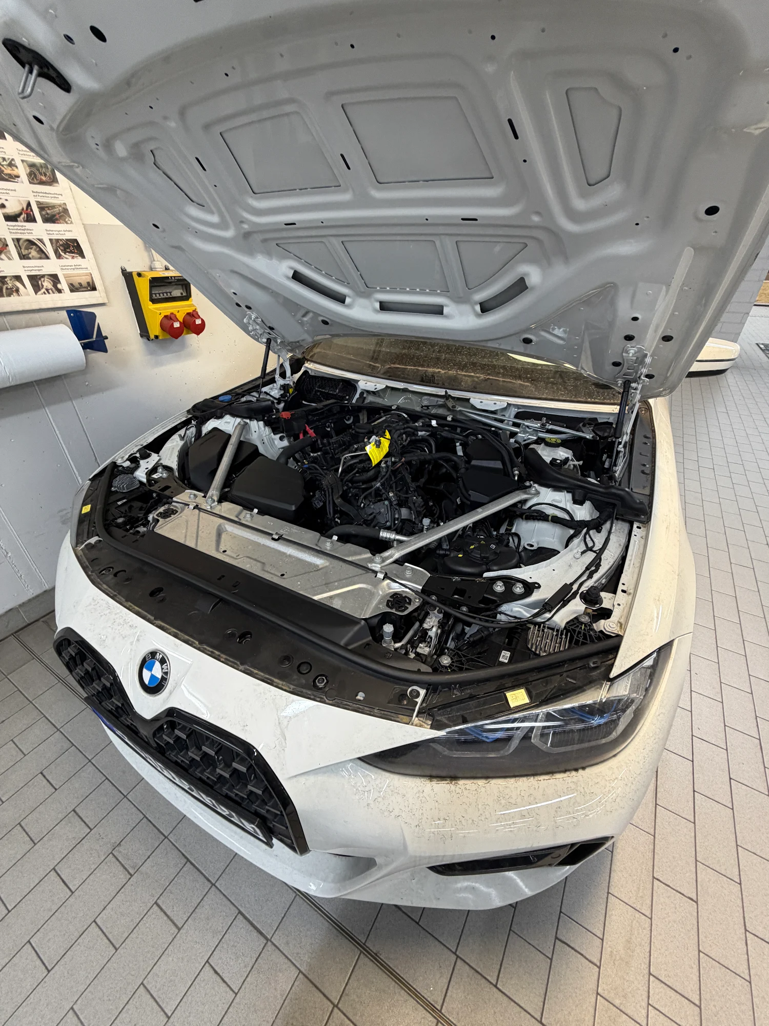 Weißer BMW mit geöffneter Motorhaube und freigelegtem Frontbereich in der Werkstatt